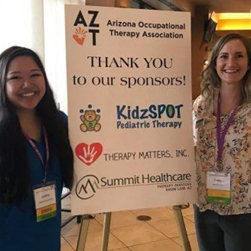 Two attendees beside a sponsor recognition display at a past conference.