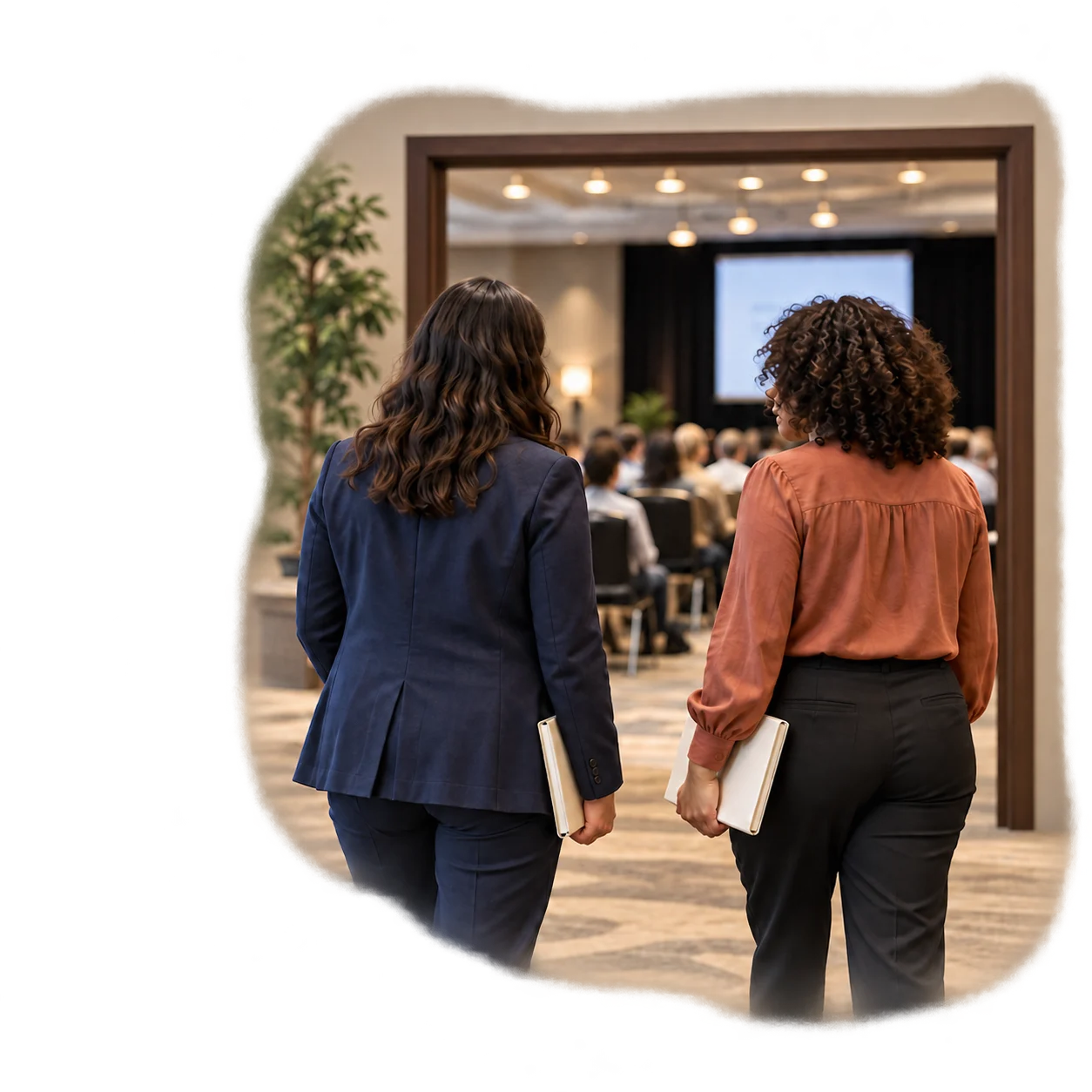 Two professionals carrying notebooks as they enter a conference auditorium.